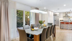 A modern dining area with a large table, chairs, and a kitchen in the background. - LA Hillside Retreat w/ Pool, Views, Fire Pit & Outdoor Lounging Casa Bellagio by Avantstay (Los Angeles)
