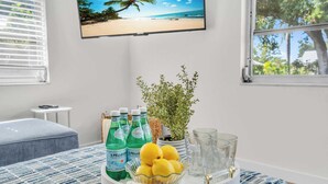 Een kamer met een bed, een klein tafeltje met drankjes en een plant, en een televisie waarop een strand te zien is.