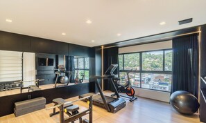 Ein modernes Fitnessstudio mit Trainingsgeräten, einem großen Spiegel und Blick auf eine Stadtlandschaft durch hohe Fenster.