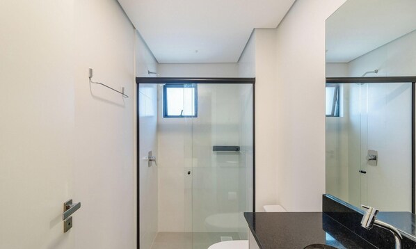Ein modernes Badezimmer mit Duschkabine aus Glas, Toilette und Waschbecken mit schwarzer Arbeitsplatte.