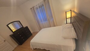 A bedroom with a bed, a dresser, a mirror, and a window with curtains. - Nature view retreat (Gatineau)
