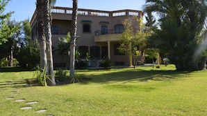 A building with a symmetrical facade, multiple balconies, and a well-maintained lawn with stepping stones. - Villa Moulay Bousselham (Marrakech)