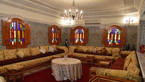 A traditional room with patterned walls, a central seating area with sofas and a round table, and decorative stained glass windows. - Villa Moulay Bousselham (Marrakech)