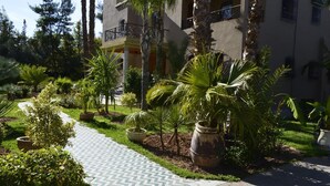 A hotel courtyard with a paved walkway, palm trees, and a building with balconies. - Villa Moulay Bousselham (Marrakech)