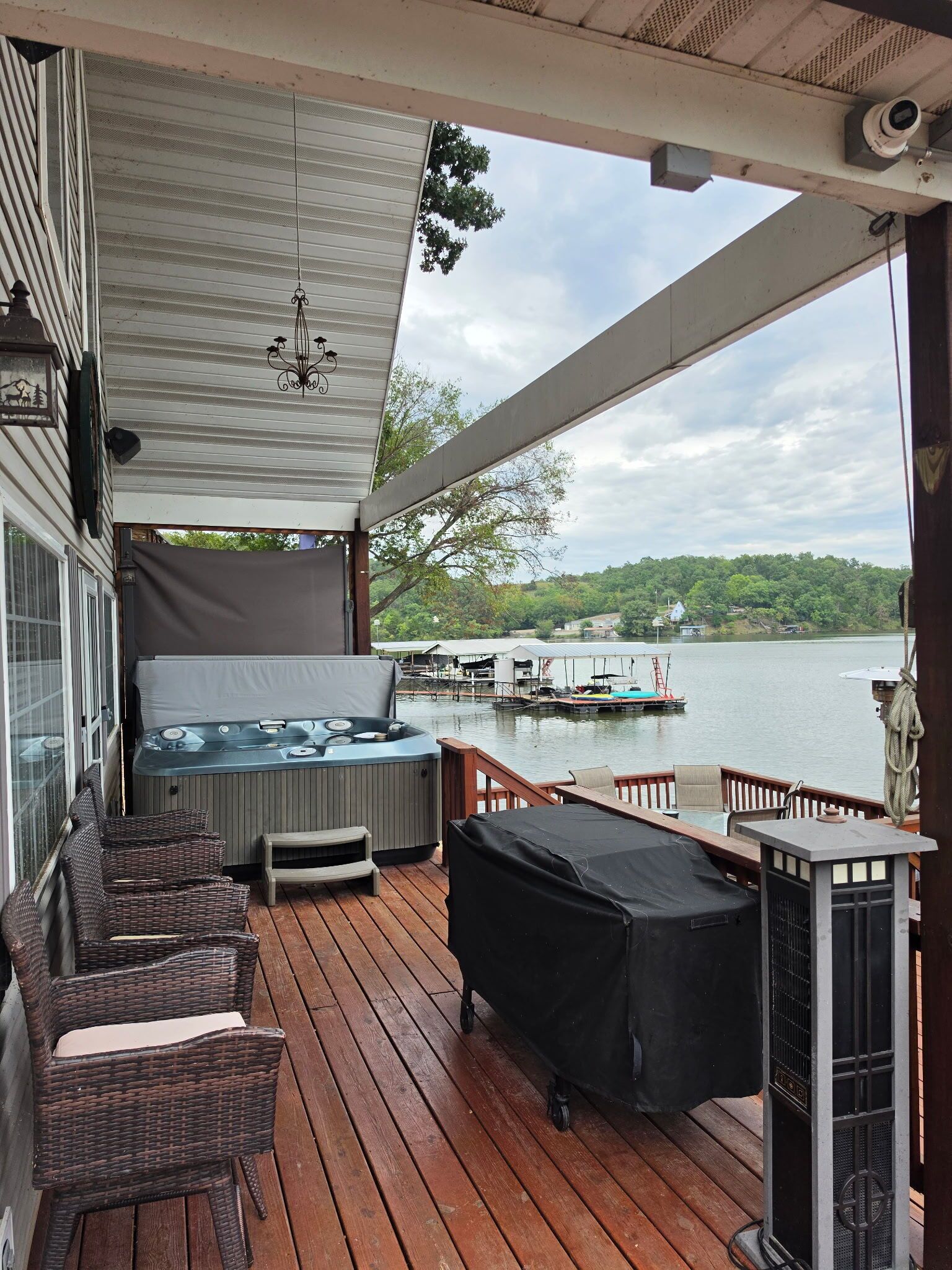 Une terrasse couverte avec des sièges d’extérieur, un barbecue et une vue sur un lac avec des quais.