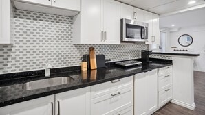 A modern kitchen with white cabinets, a black countertop, and a microwave. - Bright, New & Spacious 1 Bedroom Suite! Family friendly & central to shopping. (Burnaby)