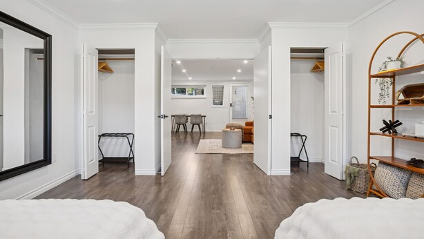 A spacious room with a large mirror, a bed, a wooden floor, and a seating area with a table and chairs. - Bright, New & Spacious 1 Bedroom Suite! Family friendly & central to shopping. (Burnaby)