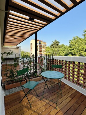Een houten terras met een tafel en stoelen, omringd door een houten hek en potplanten.
