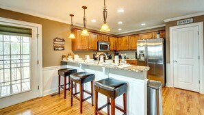A kitchen with wooden cabinets, a stainless steel refrigerator, a bar area with stools, and a sign reading "PANTRY".