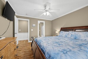 Ein Schlafzimmer mit einem Bett, einem Deckenventilator, einem Fernseher und einer Holzkommode.