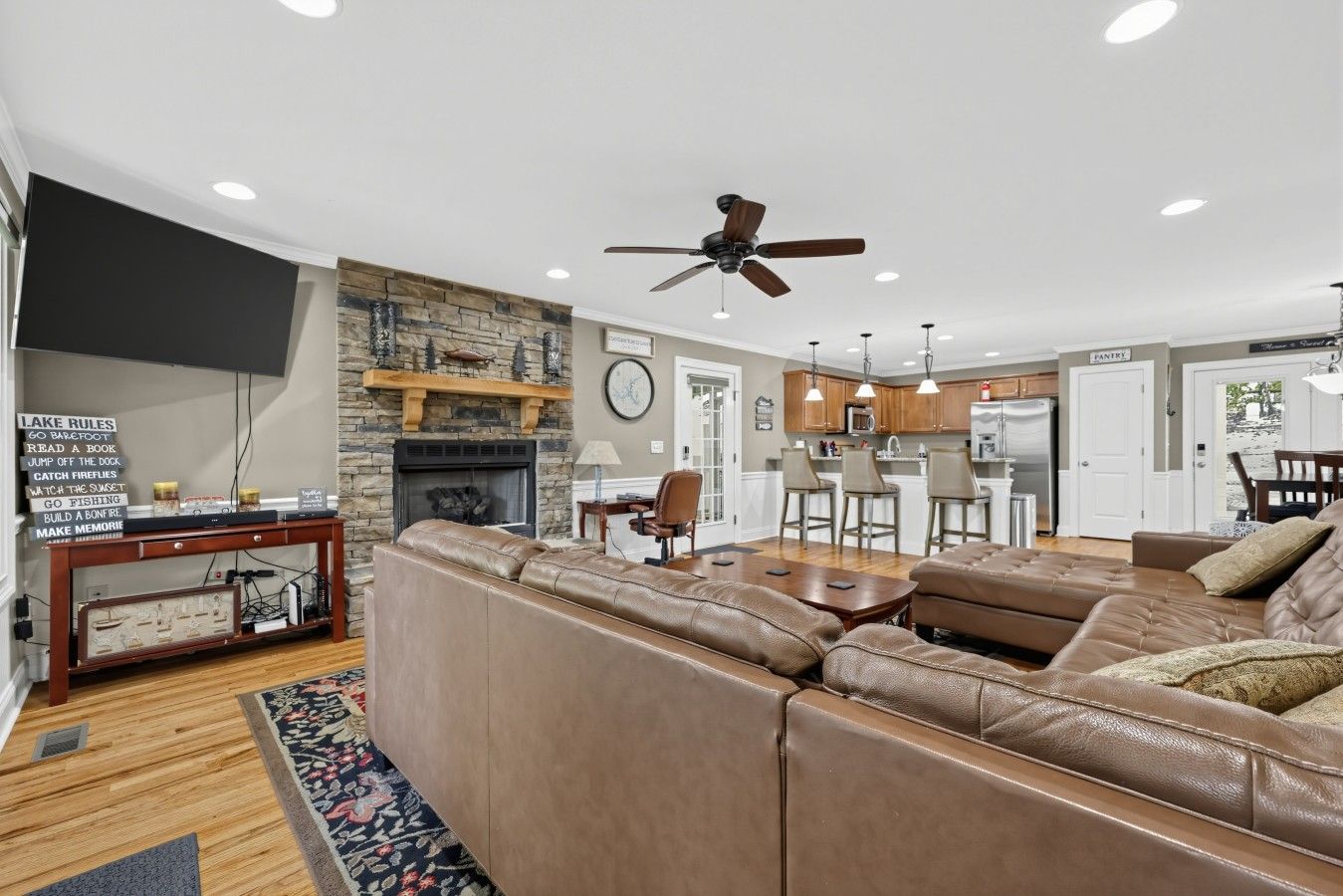 A spacious living room with a stone fireplace, leather sectional sofa, and a dining area with a kitchen in the background.