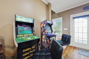 Ein Zimmer mit zwei Spielautomaten, einem schwarzen Ledersessel und einem Fenster.
