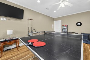 Ein Tischtennis-Tisch mit zwei roten Schlägern und einem an der Wand befestigten Fernseher.