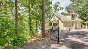 A two-story house with a porch, surrounded by trees and a gravel driveway.