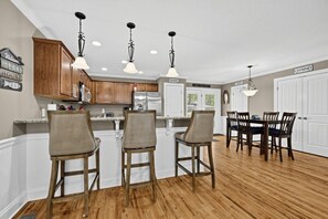 A kitchen with wooden cabinets, a refrigerator, a dining area with a table and chairs, and pendant lighting. - Lake Sinclair 4BR | Private Dock & Game Room (Sparta)
