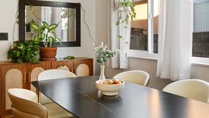 A dining area with a dark table, white chairs, a bowl of fruit, and potted plants. - Casa Malta Spa and Pool (San Diego)