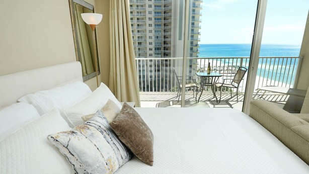 A hotel room with a large bed, a balcony with a table and chairs, and a view of the ocean. - Gulf Front 8th Floor Studio - Sleeps up to 4 (Panama City Beach)