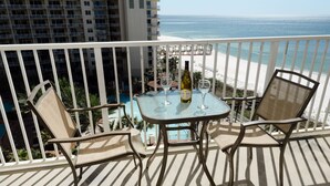A balcony with a table and chairs, a bottle of wine, and a view of the beach and ocean. - Gulf Front 8th Floor Studio - Sleeps up to 4 (Panama City Beach)
