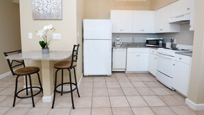A kitchen with white cabinets, a refrigerator, a stove, and a dining area with a table and chairs. - Gulf Front 8th Floor Studio - Sleeps up to 4 (Panama City Beach)
