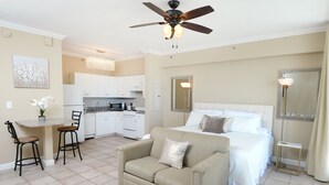 A hotel room with a bed, a sofa, a dining area with a table and chairs, a kitchen, and a ceiling fan. - Gulf Front 8th Floor Studio - Sleeps up to 4 (Panama City Beach)