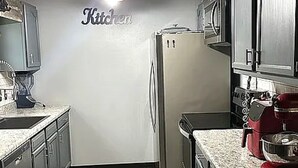 A modern kitchen with stainless steel appliances, a granite countertop, and a 'Kitchen' sign on the wall. - This house will meet all your needs (Harrison)