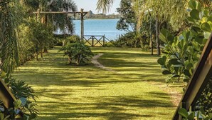 A well-maintained garden with a clear path leading to a wooden swing set overlooking a body of water. - Kite House - Ibiraquera - SC (Imbituba)