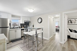 Una cocina moderna con armarios blancos, electrodomésticos de acero inoxidable y una mesa de comedor de vidrio con taburetes de bar.