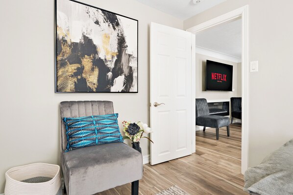 Una sala de estar moderna con un sillón gris, un cuadro abstracto en blanco y negro, y una puerta blanca que da a otra habitación.