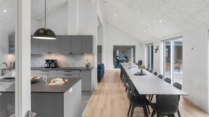 Une cuisine moderne avec des meubles gris, un îlot central et une longue table à manger entourée de chaises.