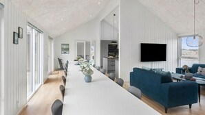 Un vaste espace de vie comprenant un grand coin repas avec une longue table, une cuisine et un téléviseur fixé au mur.
