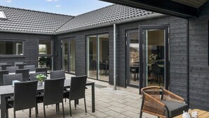 Un espace extérieur aménagé avec des tables et des chaises, un coin salon abrité et une vue sur l’intérieur.
