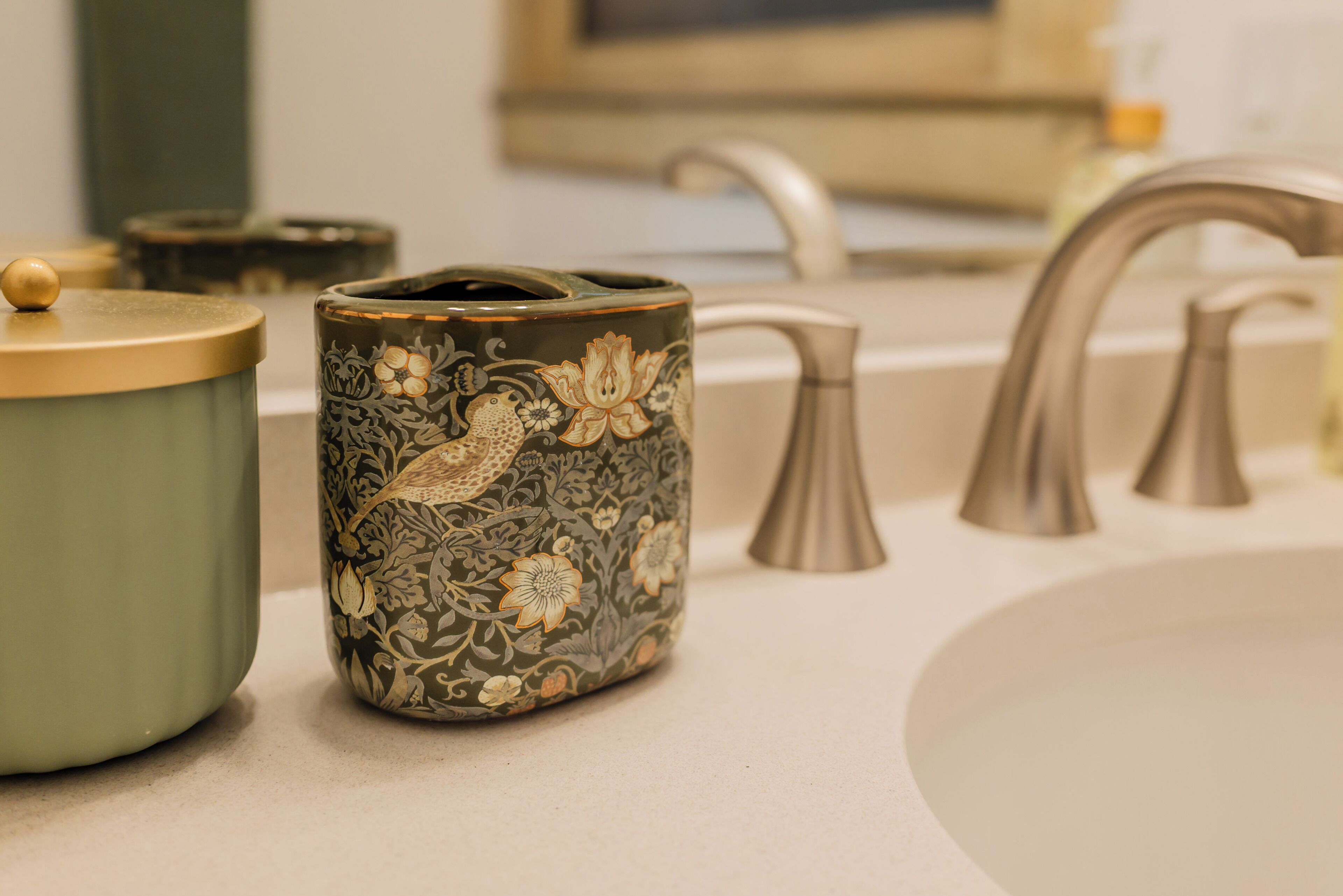 A bathroom with a sink, a green container with a lid, and a decorative jar with floral patterns.