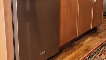 A kitchen with a stainless steel dishwasher, wooden cabinets, a granite countertop, and a patterned rug.
