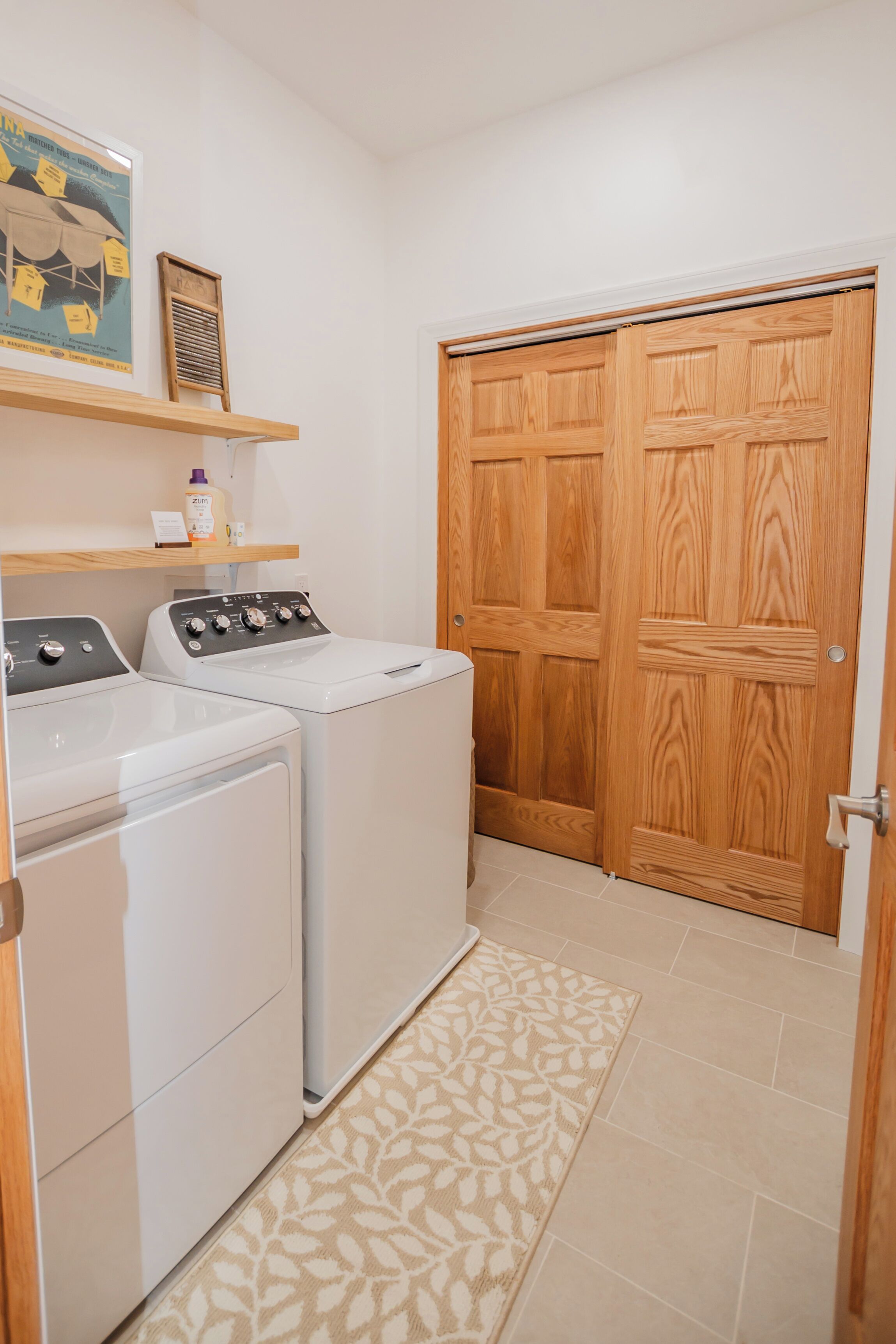 Un área de lavandería con dos lavadoras, una puerta de madera y un estante con productos de limpieza.