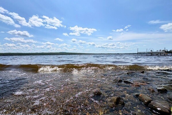A rocky shoreline with clear water and a distant pier.