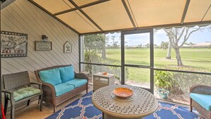 Une terrasse couverte aménagée avec des meubles en osier, une table ronde ornée d’un vase décoratif, et une vue sur un terrain de golf.