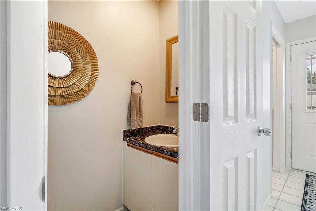 Une salle de bain avec une porte blanche, un miroir rond, une serviette beige et un lavabo doté d’un plan de travail foncé.