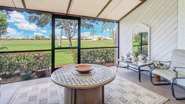 Une terrasse couverte avec une table ronde, des chaises et une vue sur un terrain de golf.