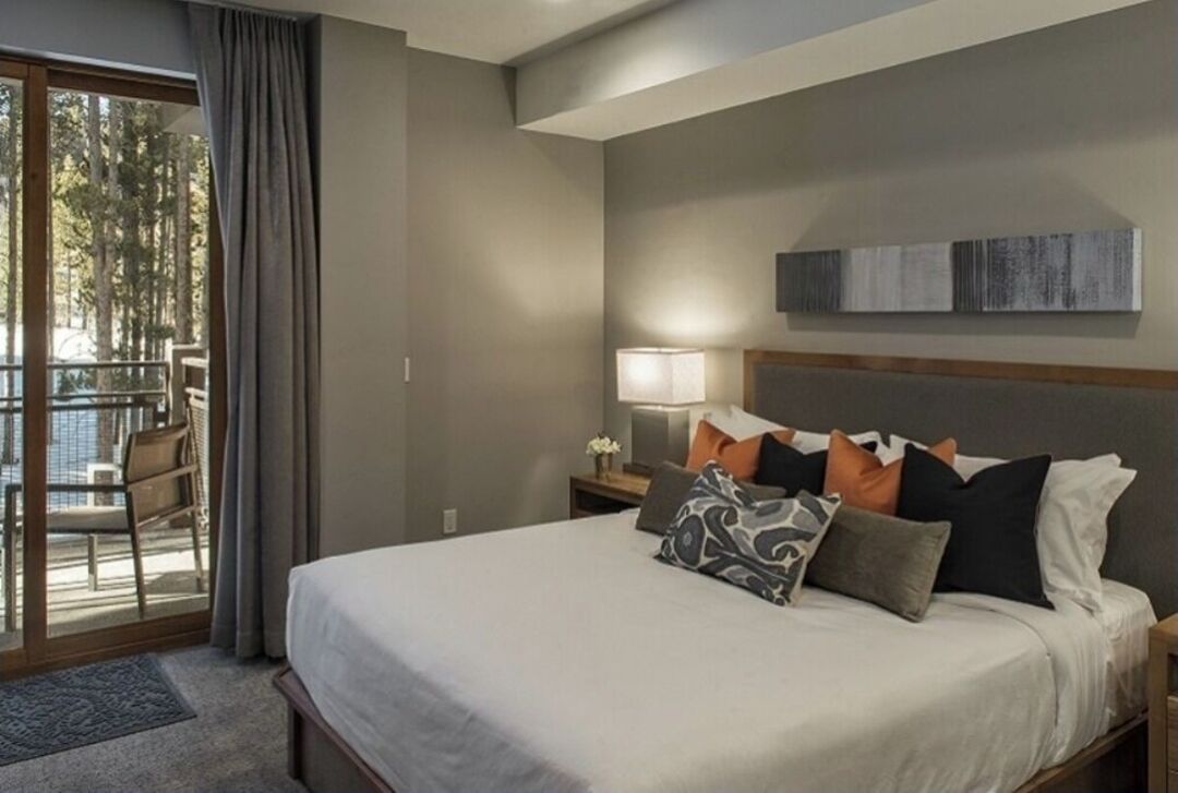 A hotel room with a bed, a nightstand, a lamp, and a view of the outdoors through a sliding door.
