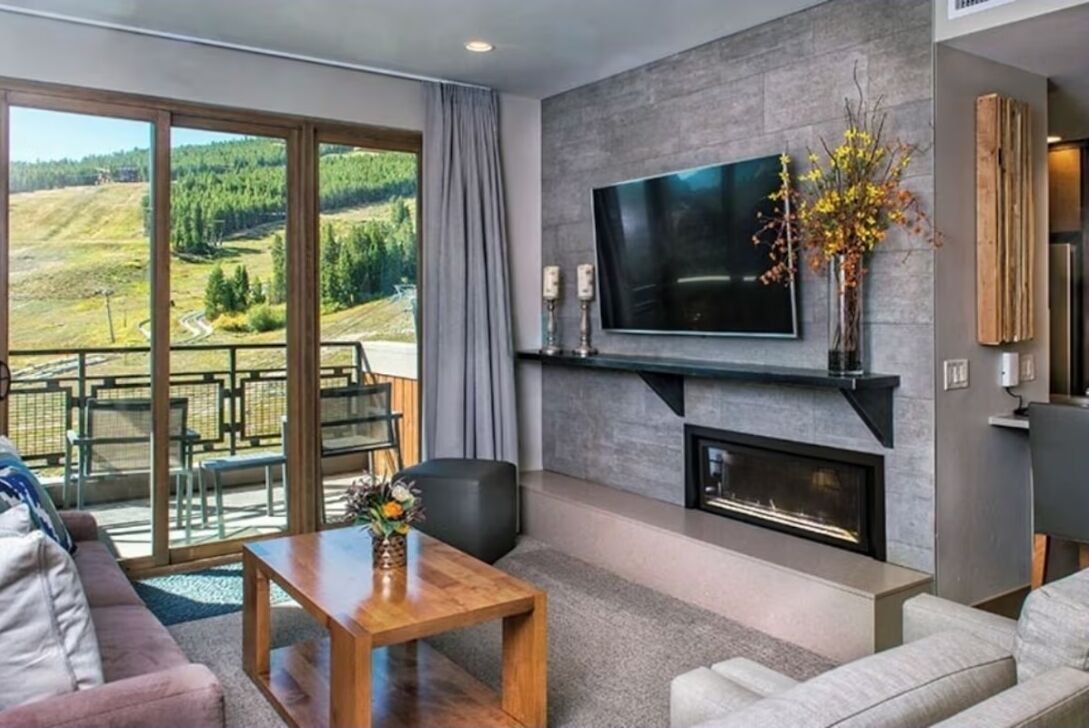 A modern living room with a fireplace, a flat-screen TV, and a balcony with a scenic view.