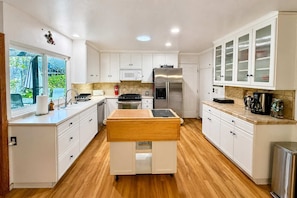 A modern kitchen with white cabinetry, a central island, stainless steel appliances, and a view of greenery outside. - Mid-Century Escape. Hot Tub. Lush Garden. A/C. Bar (Ojai)