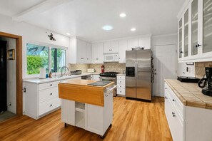 Uma cozinha moderna com armários brancos, geladeira de aço inoxidável e uma ilha de madeira.