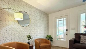 Ein Wohnzimmer mit zwei Sesseln, einem Sofa, einer Wand mit Muster und einer zur Außenseite führenden Tür.