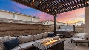 Un patio exterior con una chimenea, zona de estar y una pérgola con luces colgantes.