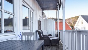 A wooden deck with a table and two wicker chairs, white railings, and a view of a red-roofed building in the background. - Awesome apartment in Lindesnes with WiFi (Lindesnes)
