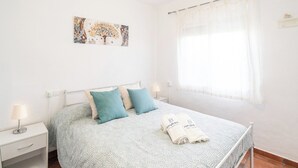 Una cama con ropa de cama estampada, dos almohadas y una toalla doblada sobre una estructura de metal blanco.