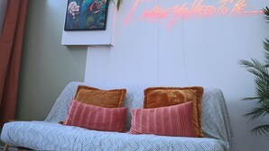 Una sala de estar moderna con un sofá que tiene cojines estampados, un letrero de neón montado en la pared y una obra de arte enmarcada.