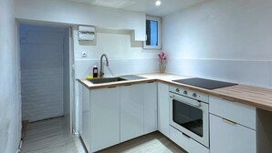 Una cocina compacta con armarios blancos, horno empotrado, lavabo y ventana sobre el lavabo.