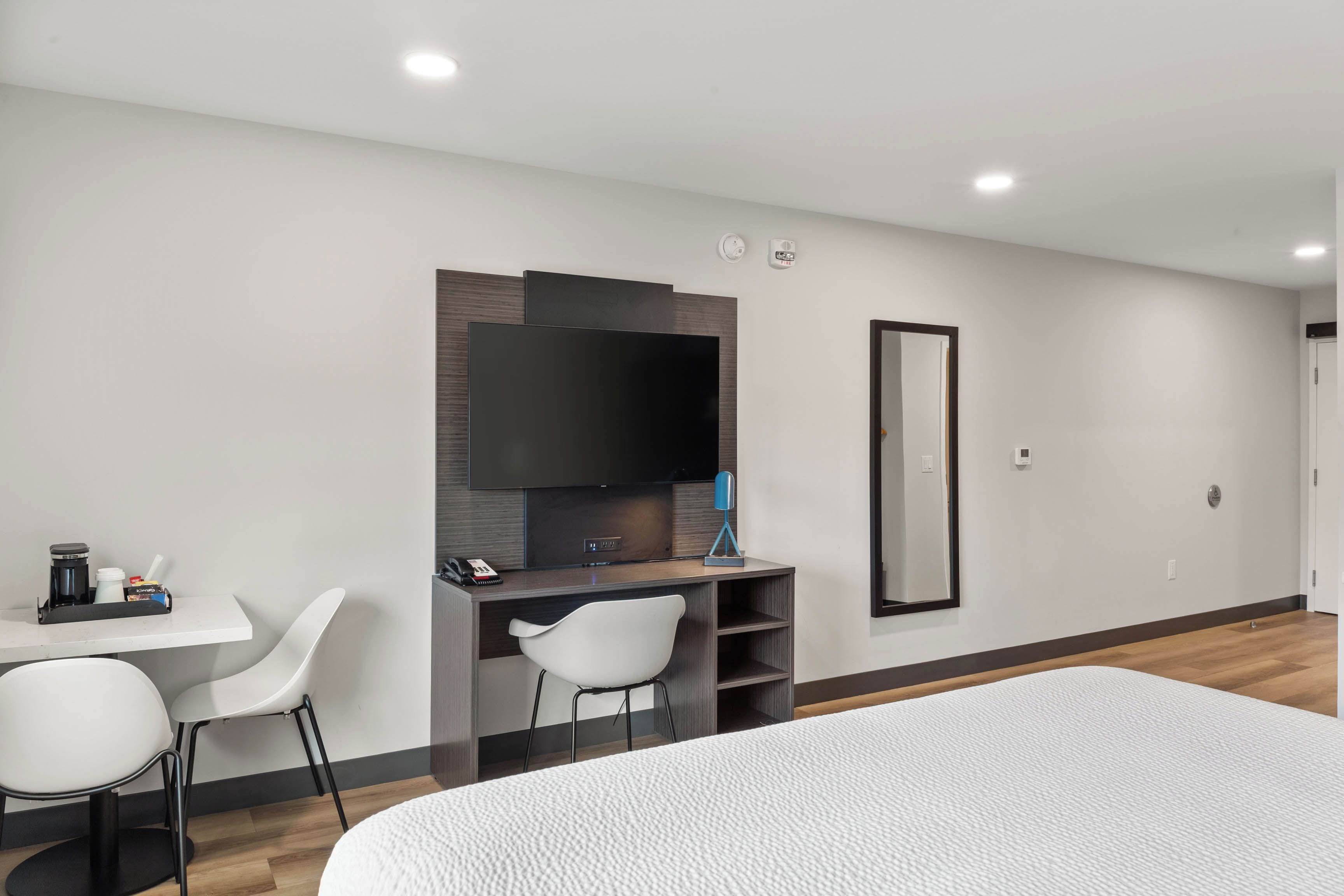 Ett hotellrum med en säng, ett skrivbord med en stol, en platt-TV och en spegel.