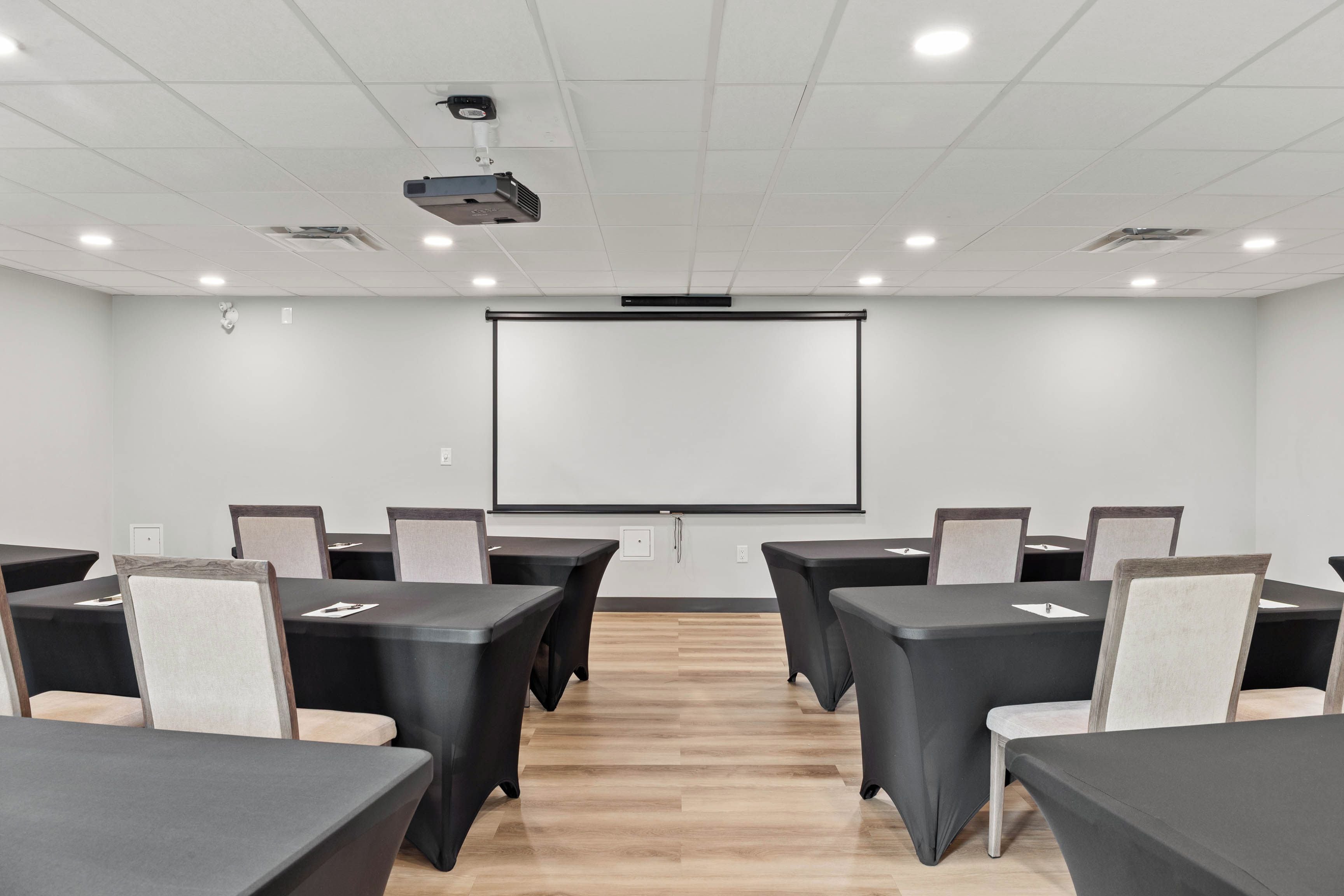 A conference room with a projector, a white screen, and multiple tables with chairs.